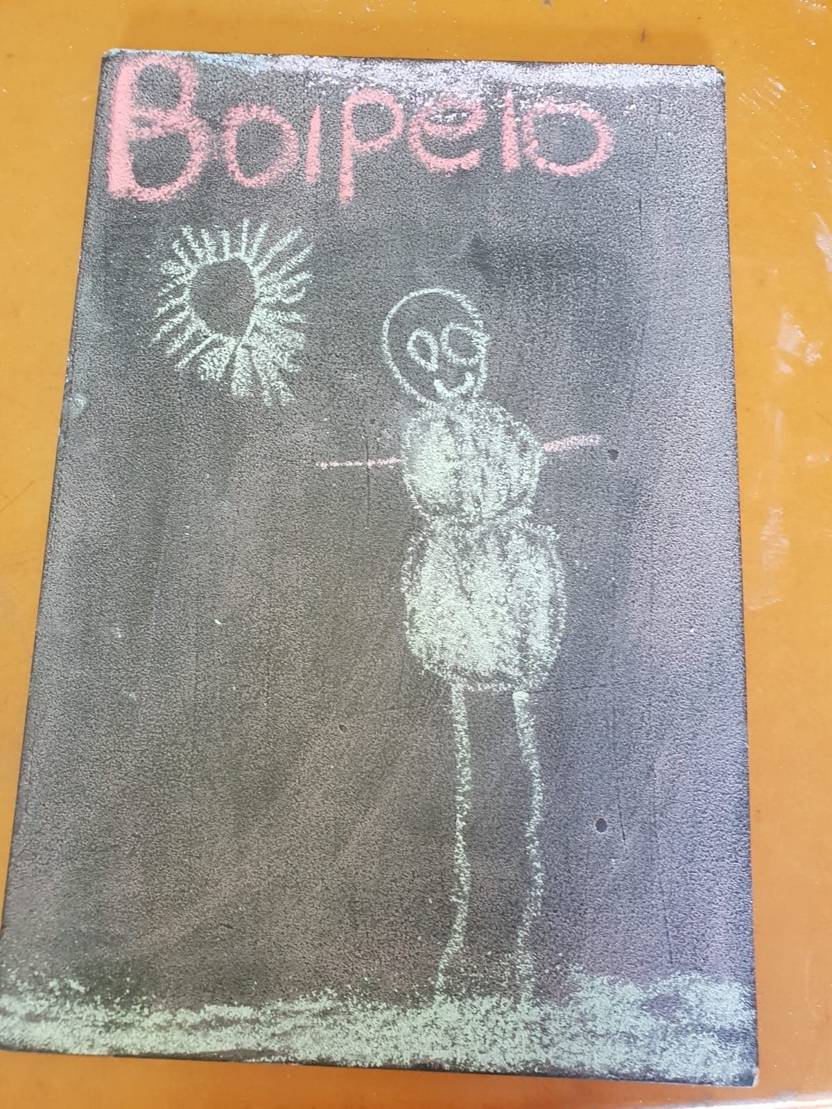 A chalkboard self-portrait drawn by a Tiny Town child, signed Boipelo, with a bright sun