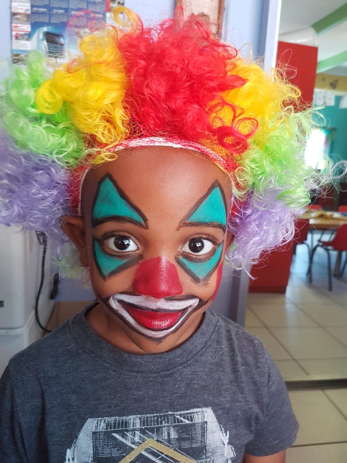 A Tiny Town child in full clown face paint and a rainbow wig on a dress-up day