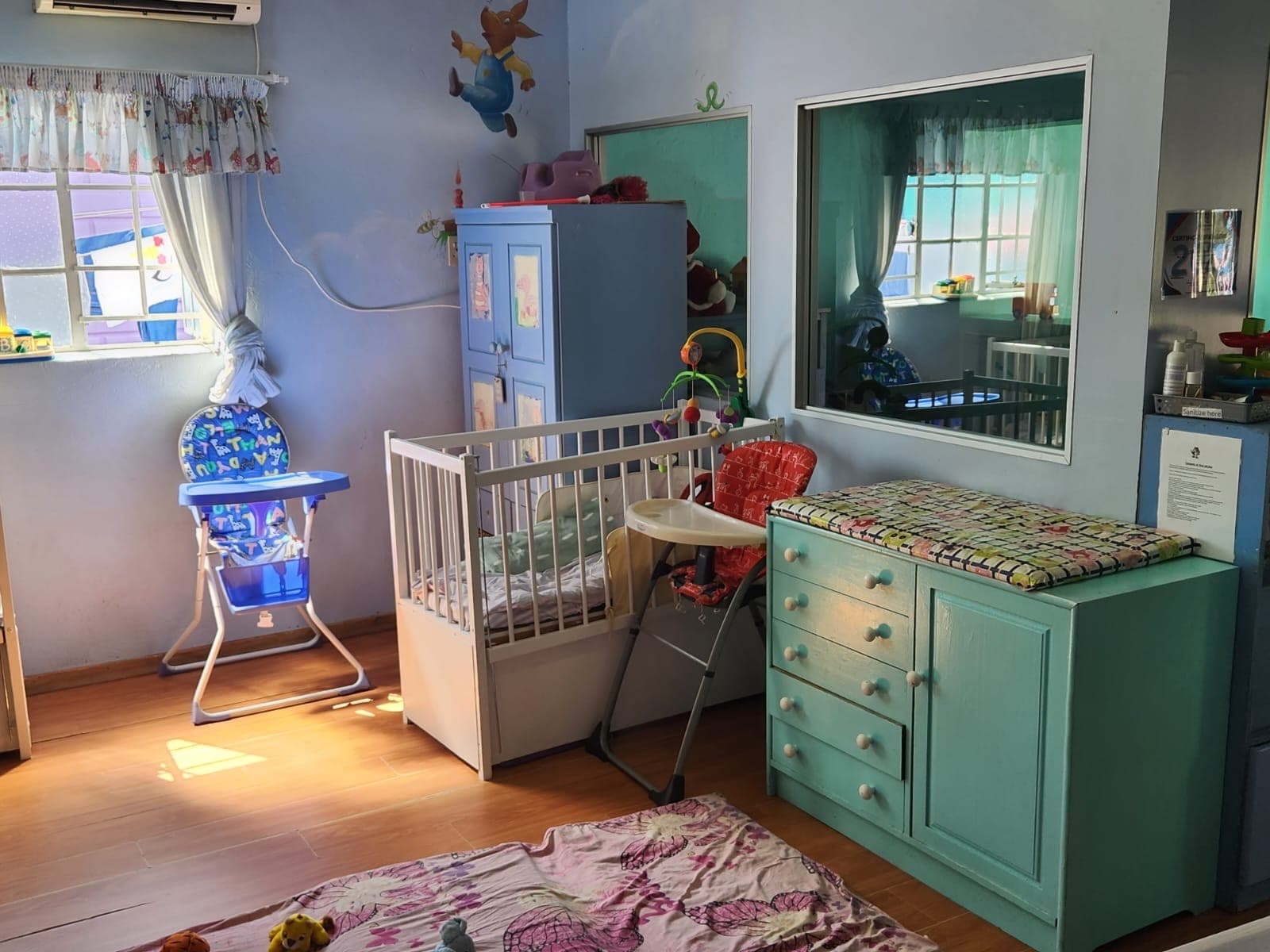A Tiny Town nursery room with a cot and changing dresser against soft teal walls
